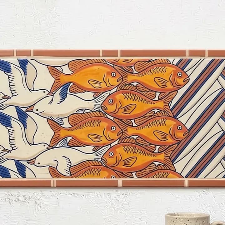 Glazed tile detail of white birds flying into a shoal of orange fish, beside blue and cream stripes.
